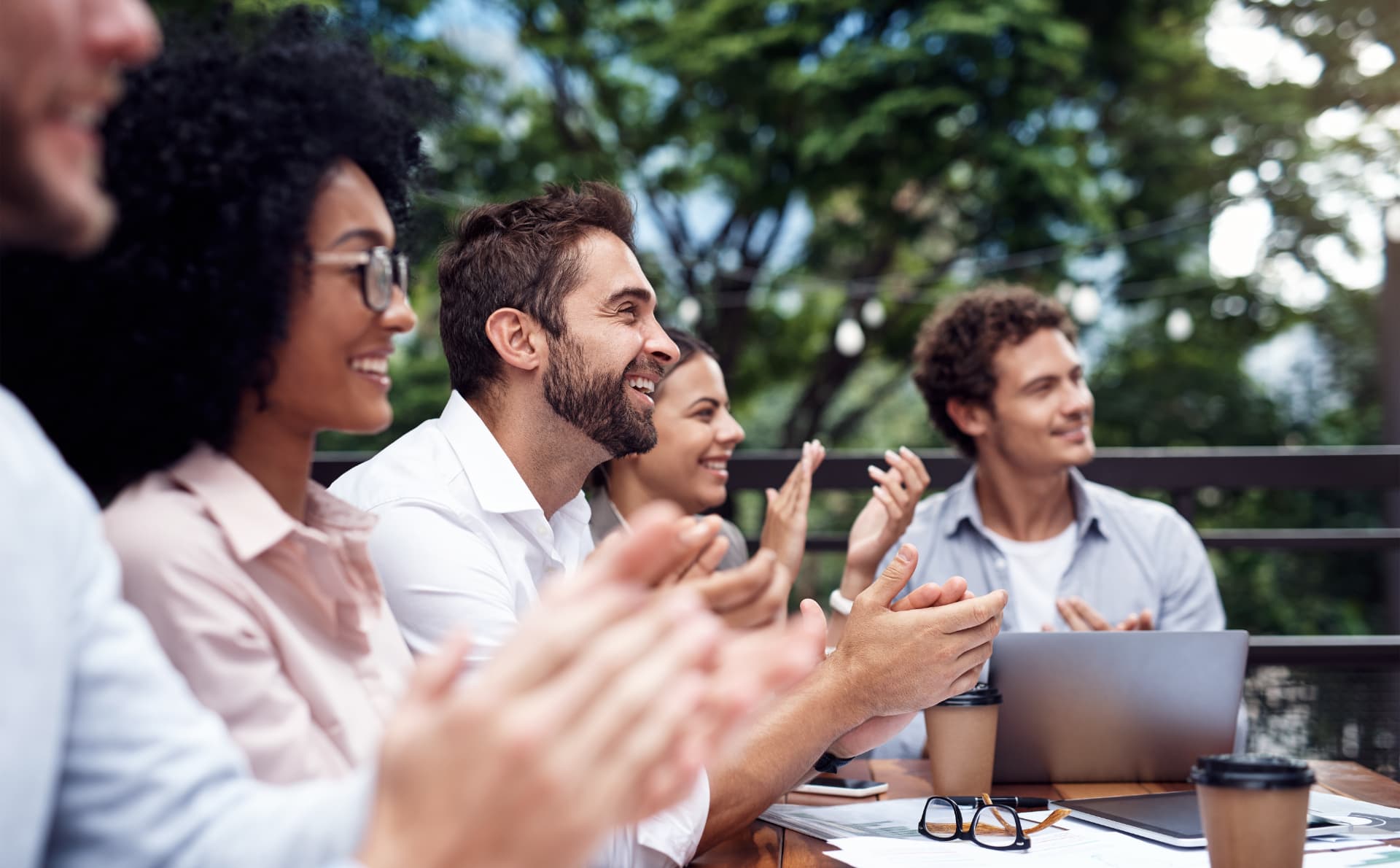 A group of colleagues seated outdoors, smiling and applauding together